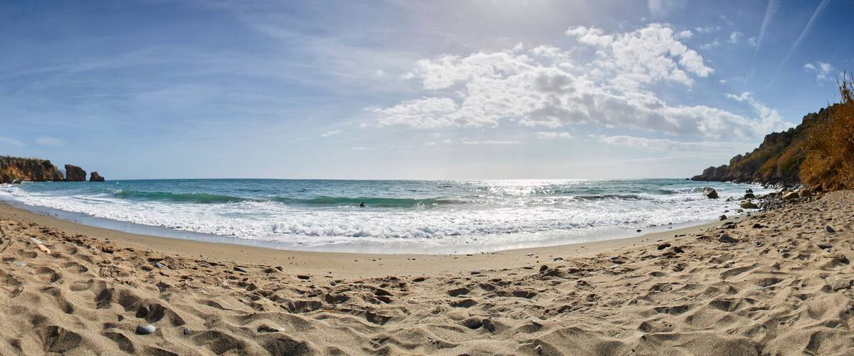 A sandy beach with waves, rocky cliffs, and a clear sky.