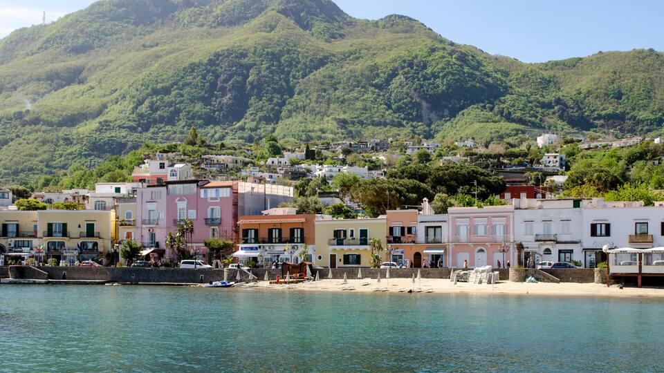 A coastal town with colorful buildings, a beach, and a mountain in the background.