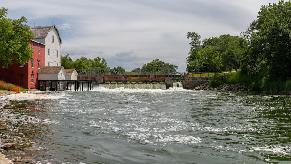 A river with a dam, a wooden bridge, and a red building.