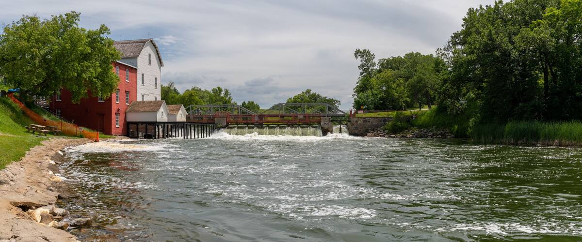 A river with a dam, a wooden bridge, and a red building.