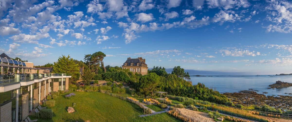 A coastal landscape with a large house, a grassy area, and a rocky shoreline.