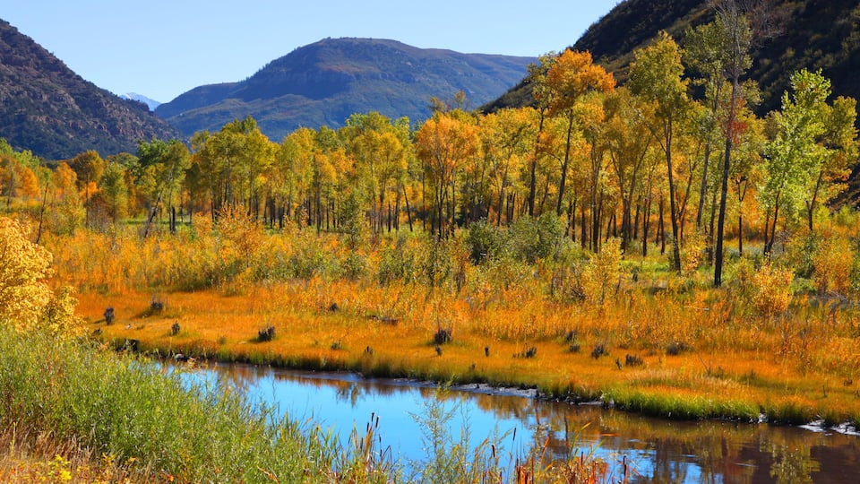 A river surrounded by autumn-colored trees and hills in the background.