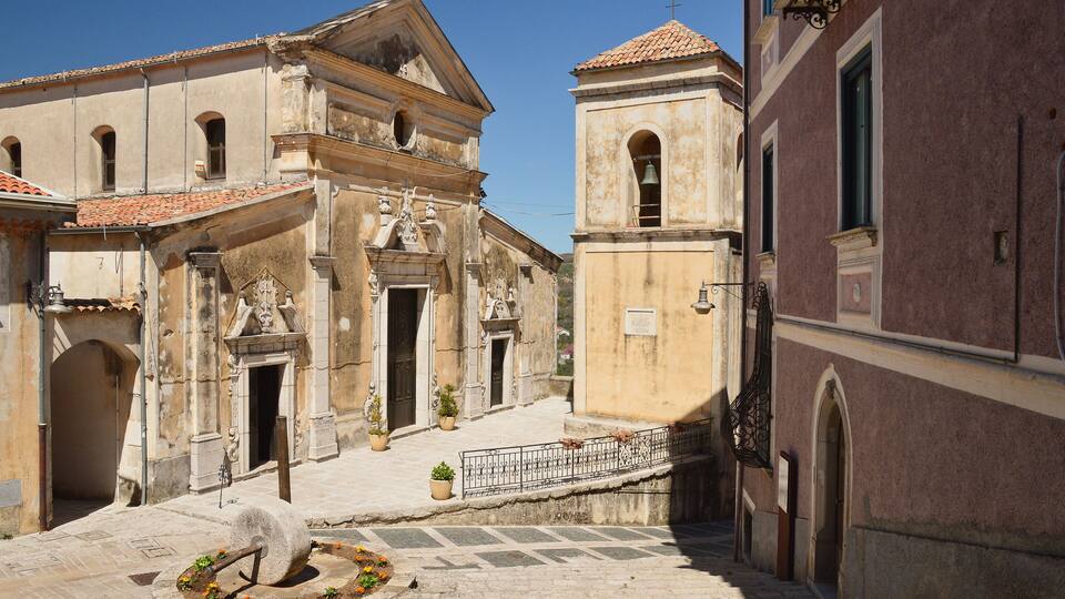 An old church with a bell tower, a fountain, and a paved courtyard.