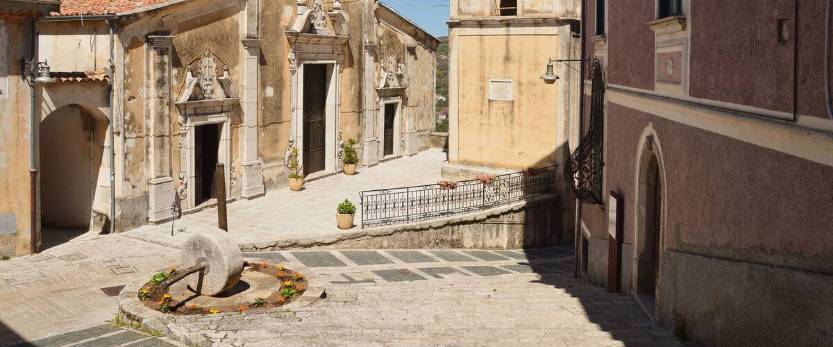 An old church with a bell tower, a fountain, and a paved courtyard.