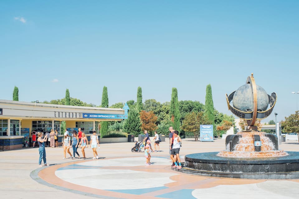 Une place publique avec une fontaine, des gens qui se promènent et un bâtiment portant une enseigne.