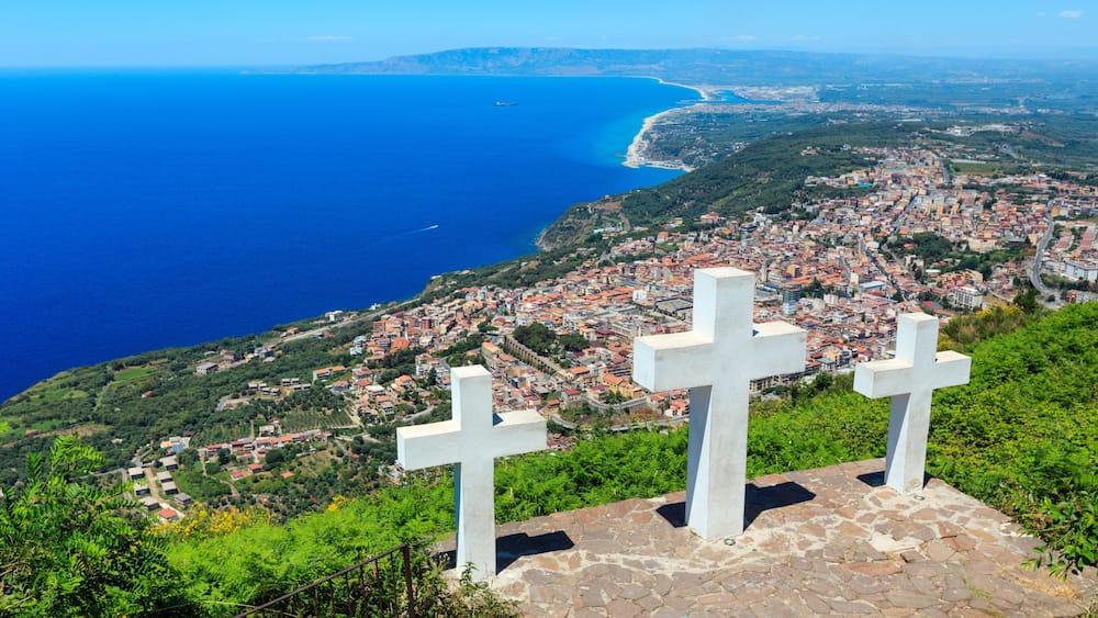 Eine Küstenstadtansicht mit Blick aufs Meer und zwei weiße Kreuze auf einer Steinterrasse.