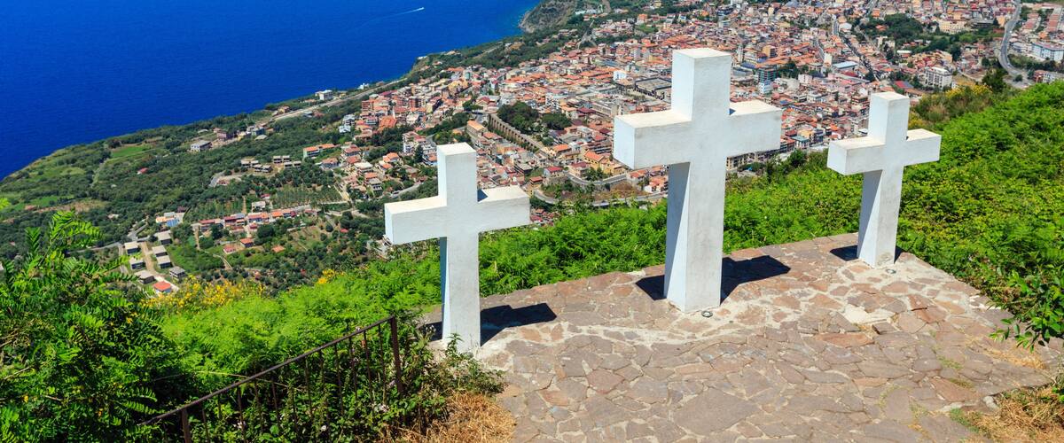 A coastal cityscape with a view of the sea and two white crosses on a stone platform.