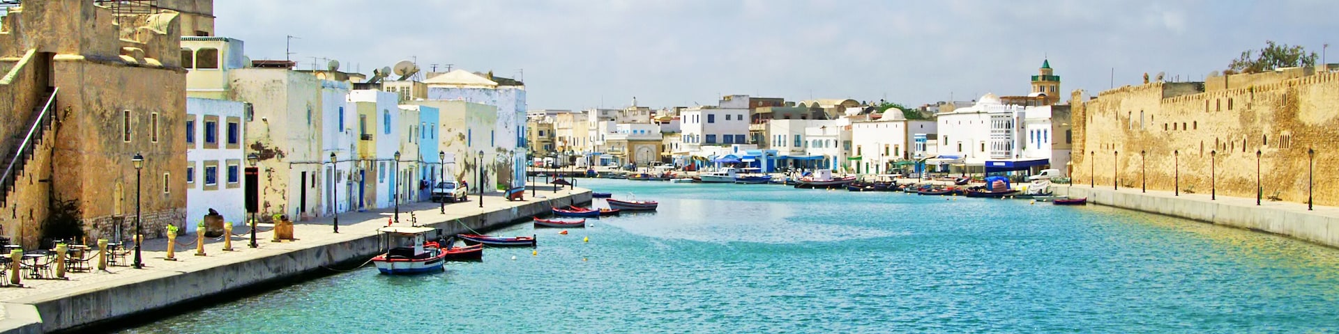 A coastal town with a clear blue harbor, historic buildings, and a fortified wall.