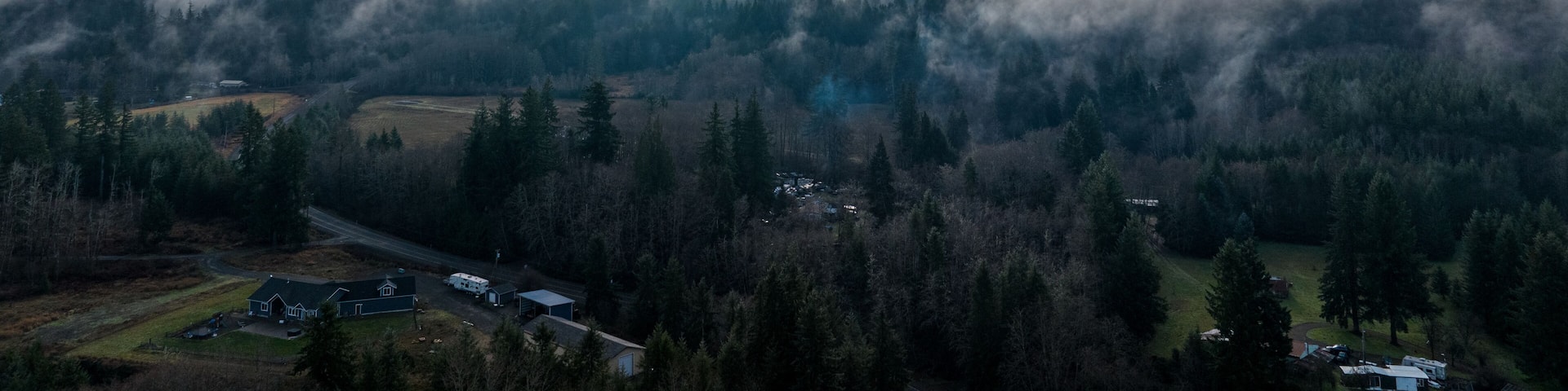 Aerial view of twin cooling towers emerge through the dense fog, piercing the skyline above verdant forest, Elma, Washington, United States.