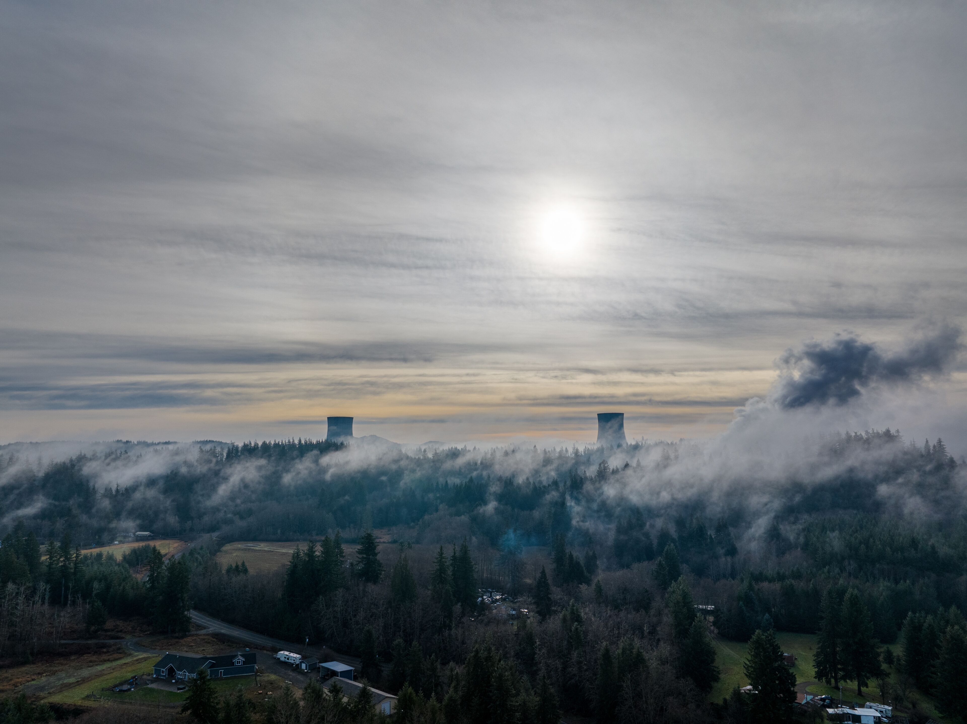 A landscape with two cooling towers, a road, and a forested area.