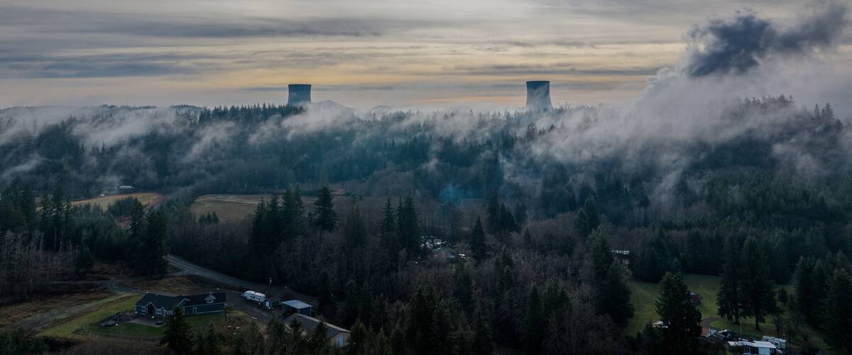 A landscape with two cooling towers, a road, and a forested area.