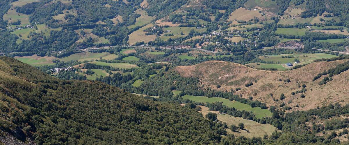 A mountainous landscape with rolling hills, dense forests, and scattered buildings.
