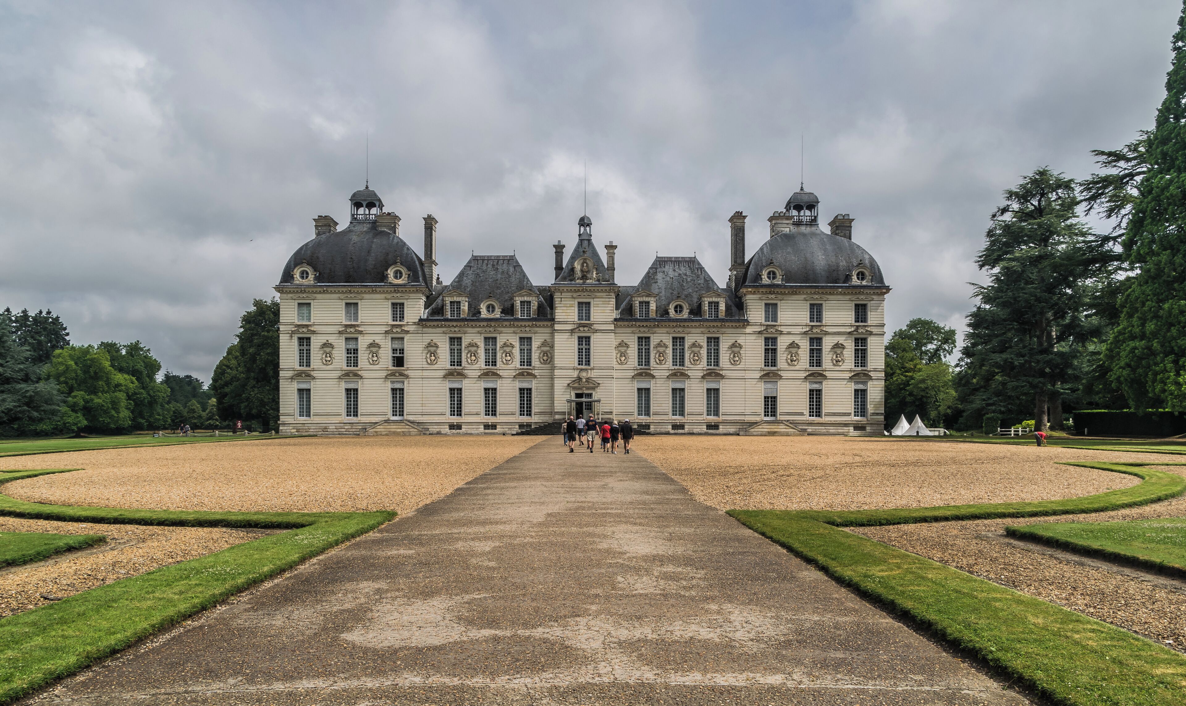 A large, historic building with symmetrical architecture, a central dome, and a formal garden with a gravel path leading to the entrance.