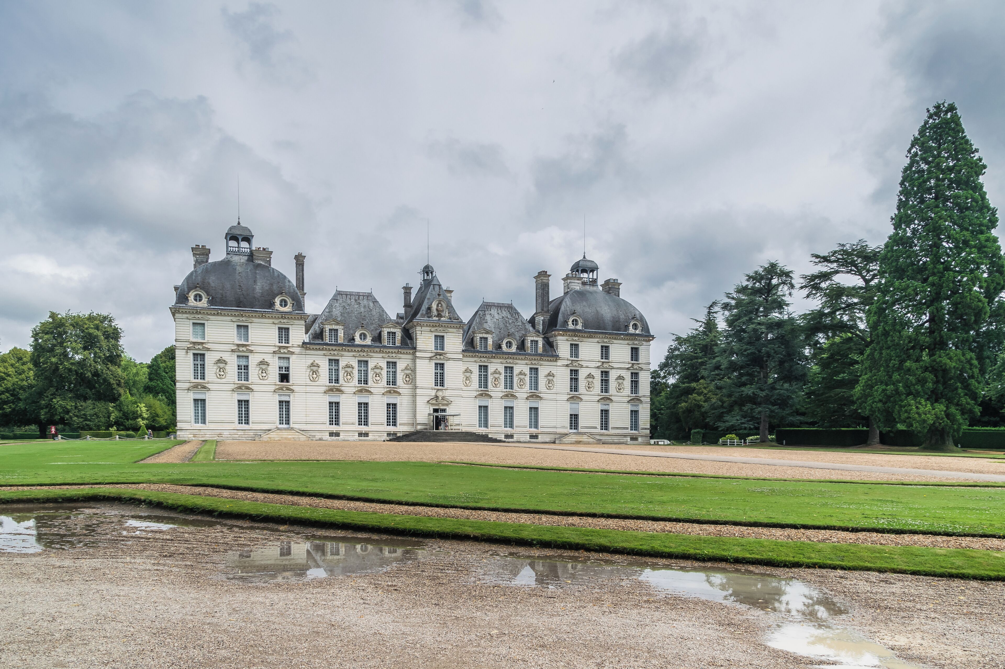 A large, historic building with multiple domes and towers, surrounded by well-manicured lawns and a reflecting pond.