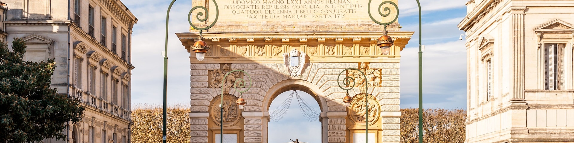 Um arco imponente com inscrições, ladeado por edifícios clássicos, sob um céu claro.