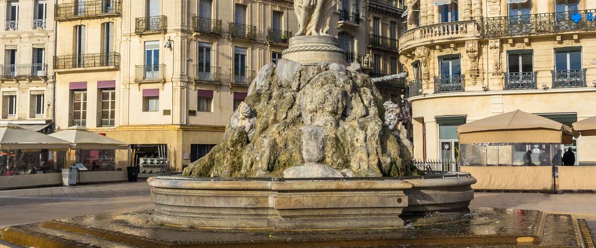 Una fuente con una estatua, rodeada de edificios históricos con balcones y una cúpula.