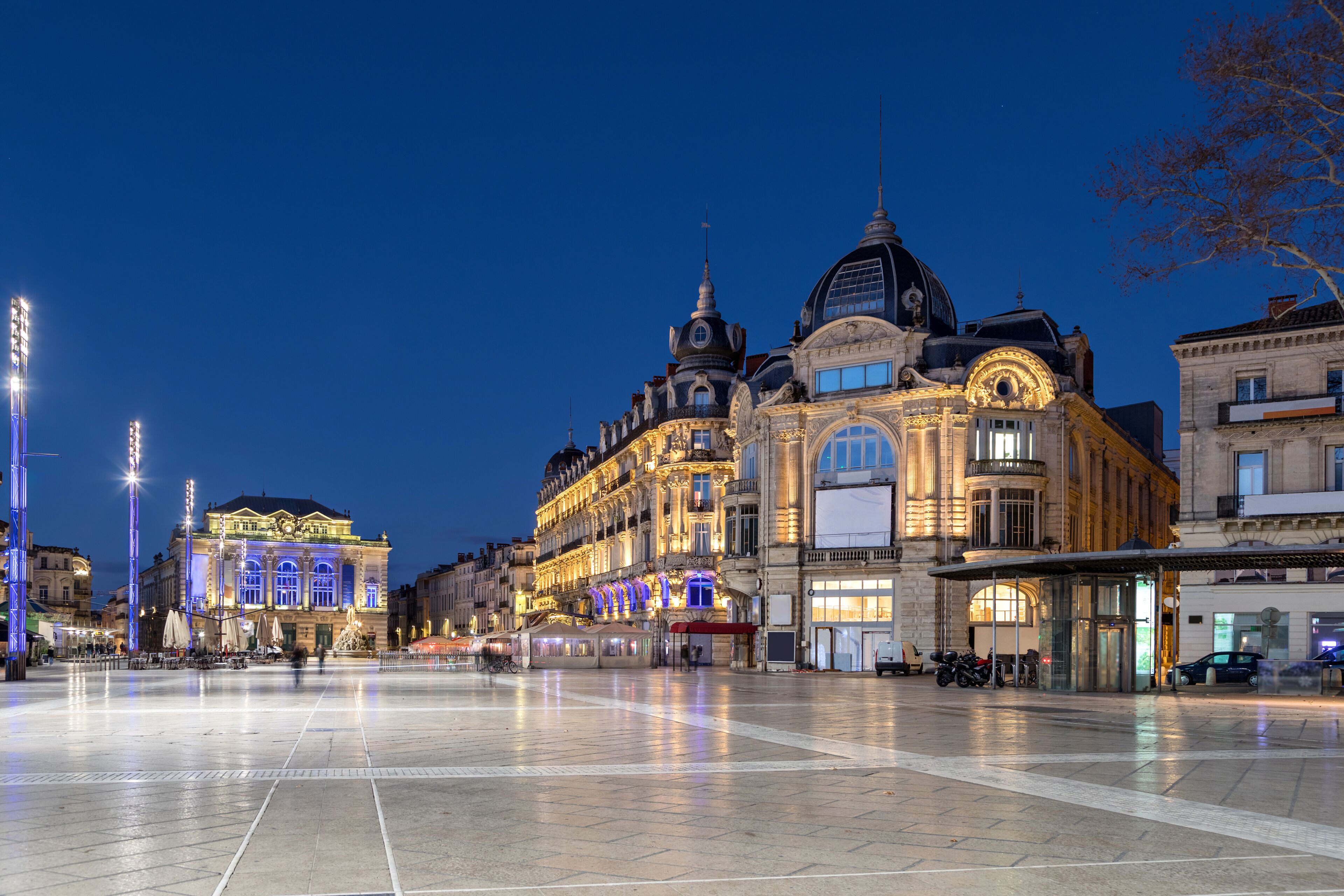 A historic building with ornate architecture, a plaza with a fountain, and a tram line.
