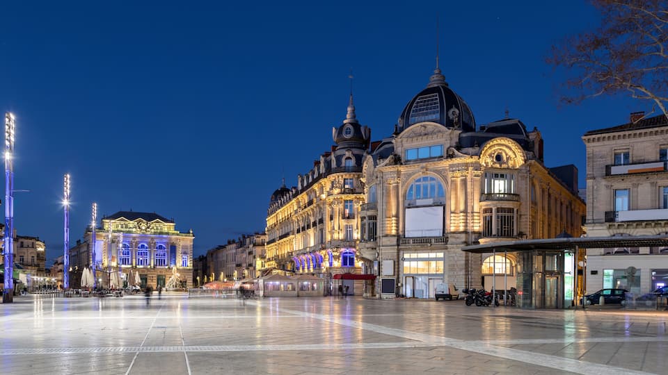 A historic building with ornate architecture, a plaza with a fountain, and a tram line.