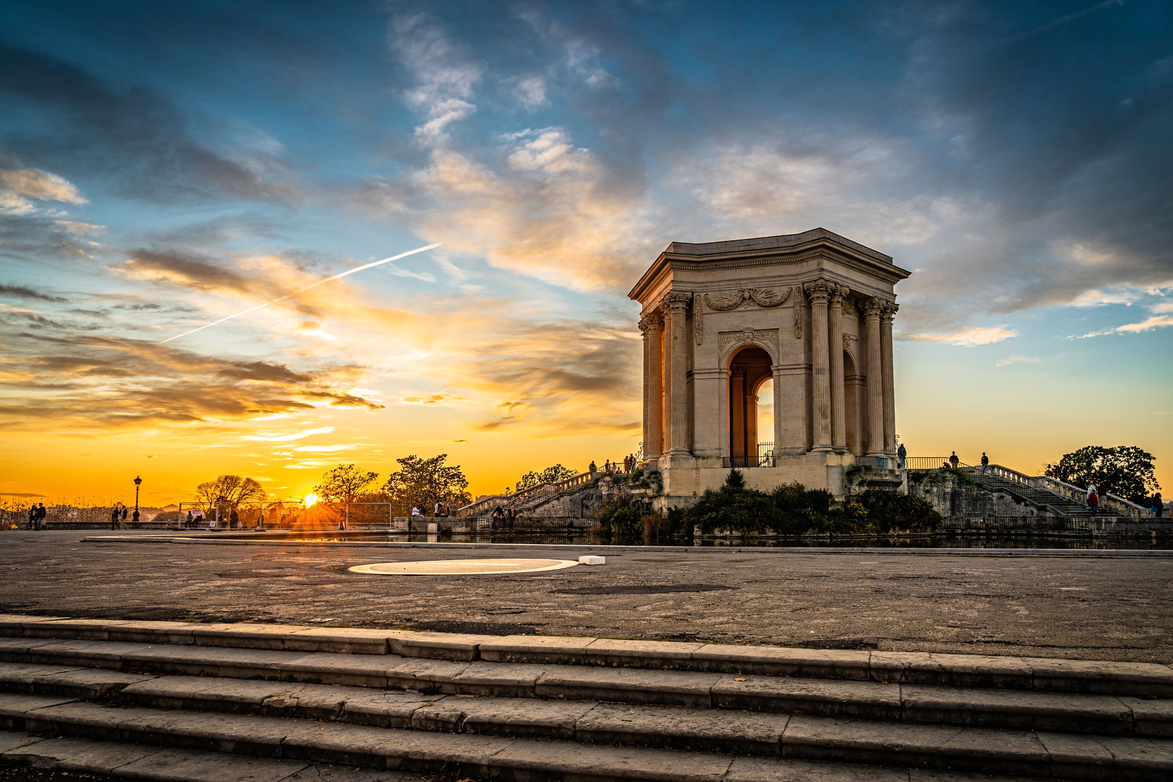 A grand arch monument with steps leading up to it, set against a sunset sky.