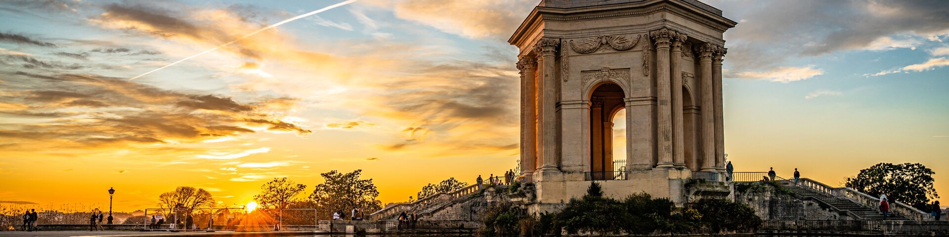 A grand arch monument with steps leading up to it, set against a sunset sky.