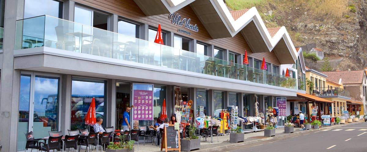 A coastal restaurant with outdoor seating, red umbrellas, and a cliffside view.