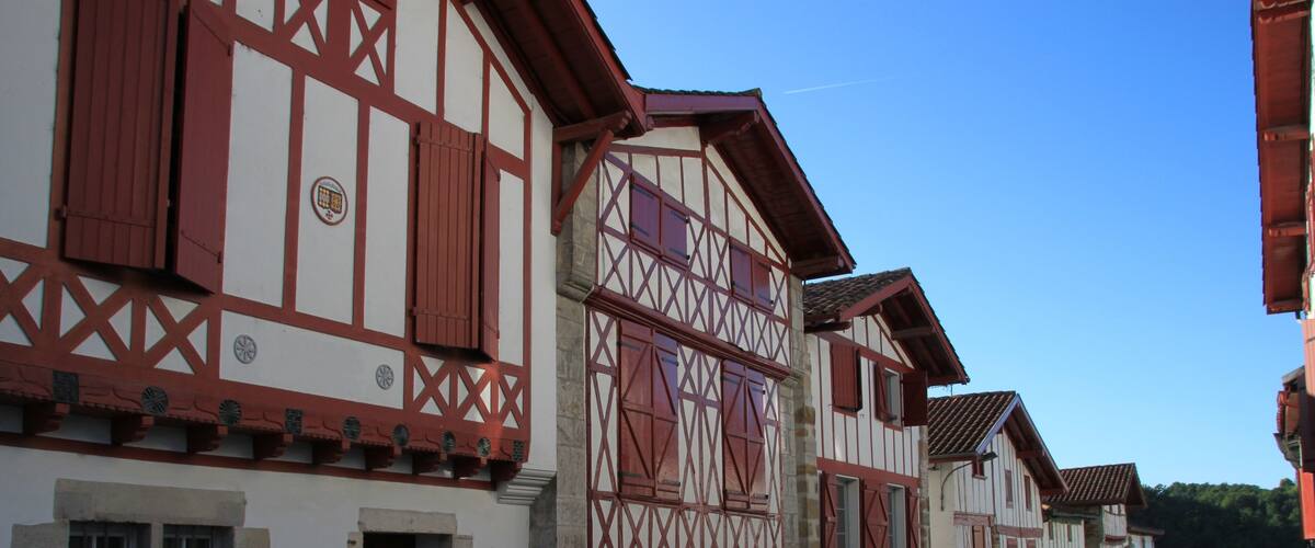A row of traditional half-timbered buildings with red and white facades, set against a clear blue sky.