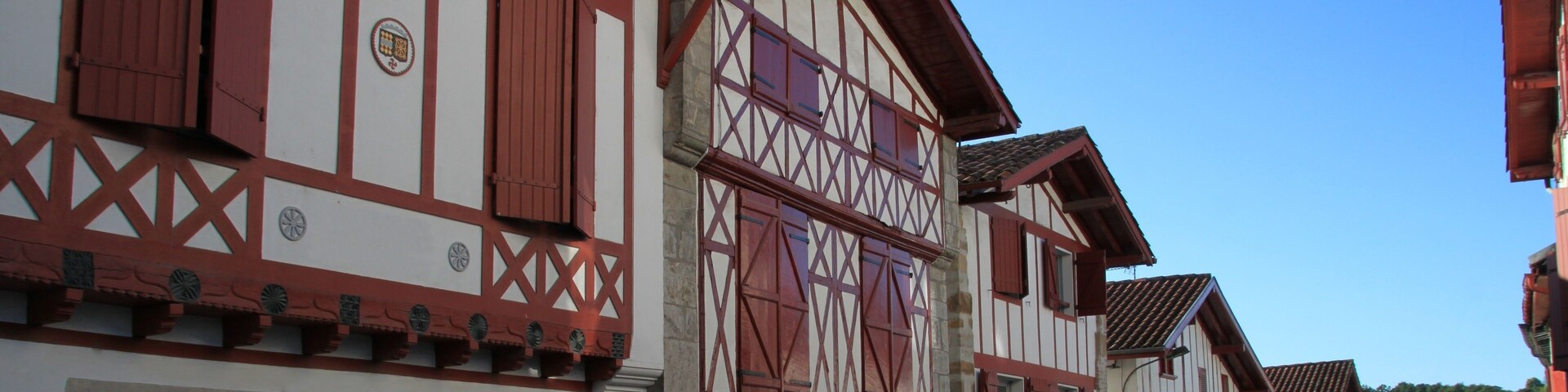 A row of traditional half-timbered buildings with red and white facades, set against a clear blue sky.