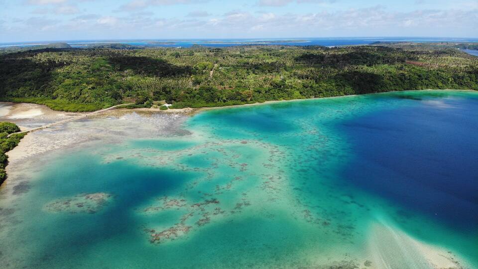 An aerial view of a coastal area with clear turquoise waters, sandy beaches, and dense green vegetation.