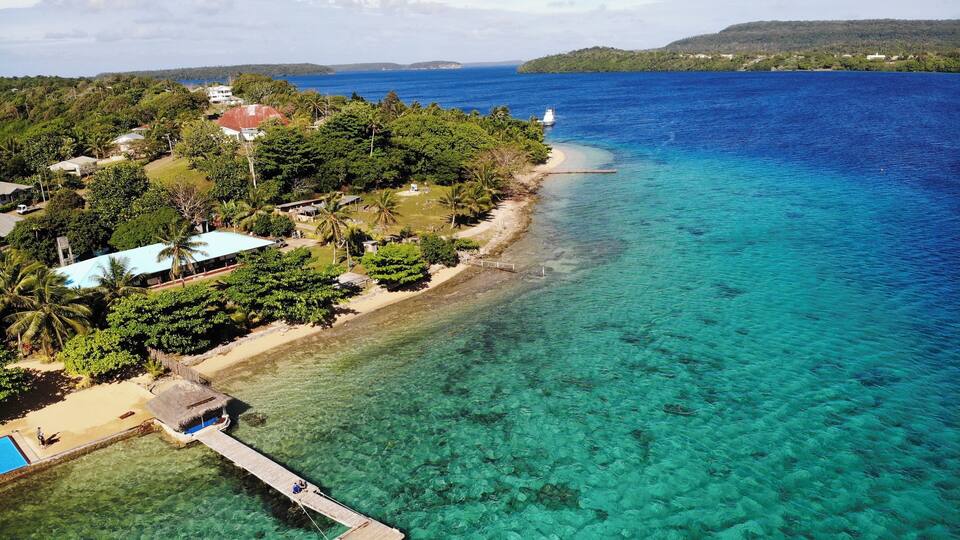 A tropical island with clear turquoise waters, a wooden pier, and lush greenery.