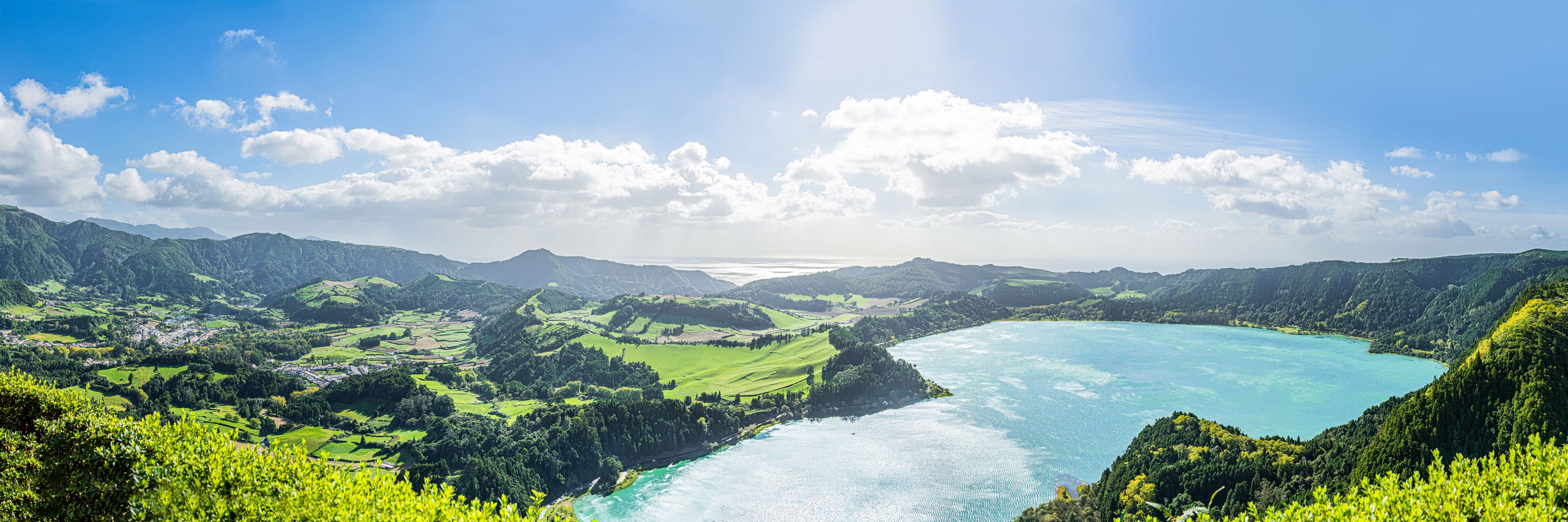 A coastal landscape with green fields, a river, and a turquoise bay.