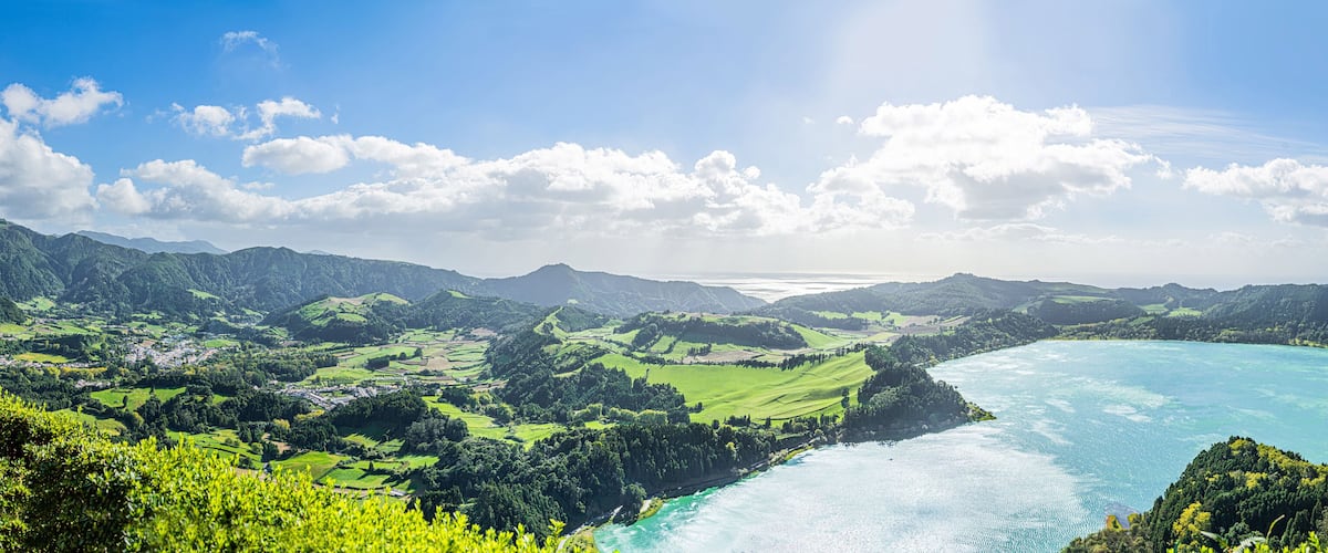 A coastal landscape with green fields, a river, and a turquoise bay.