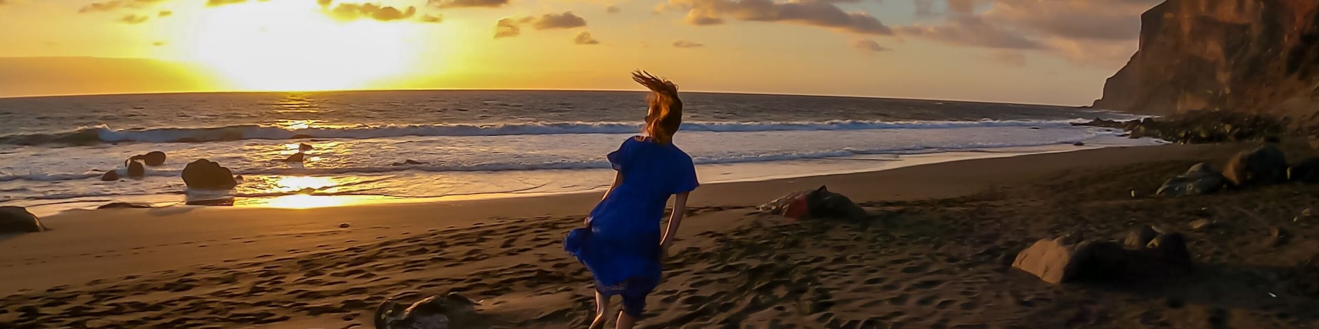 Una playa con olas, un atardecer y un acantilado.