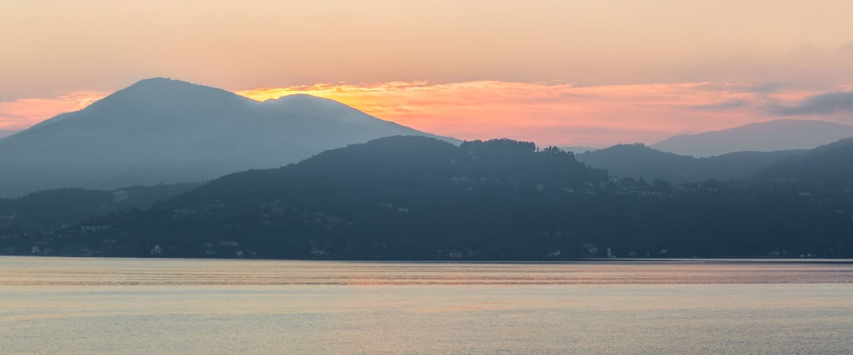 A mountain range at sunset with calm water in the foreground.