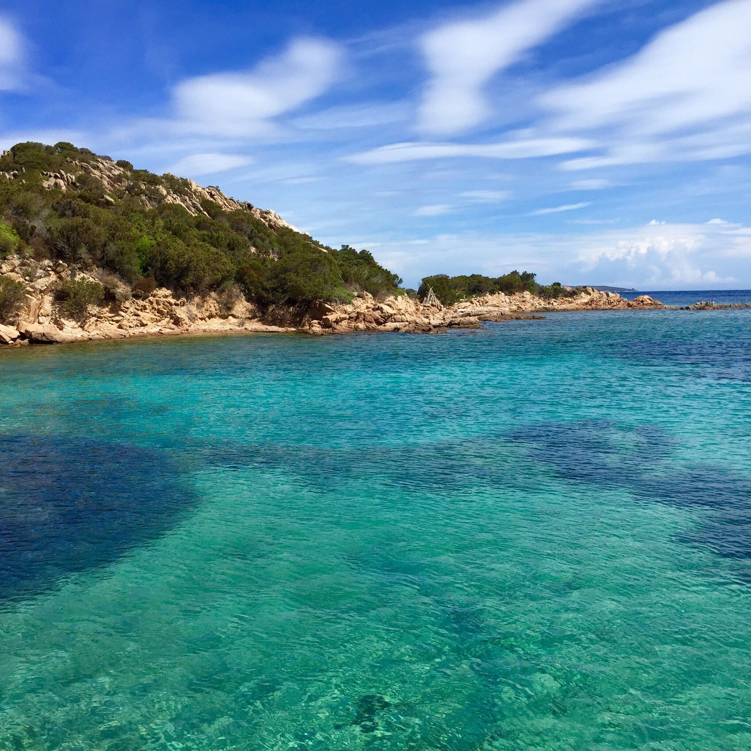A coastal landscape with clear turquoise waters, rocky cliffs, and dense green vegetation.