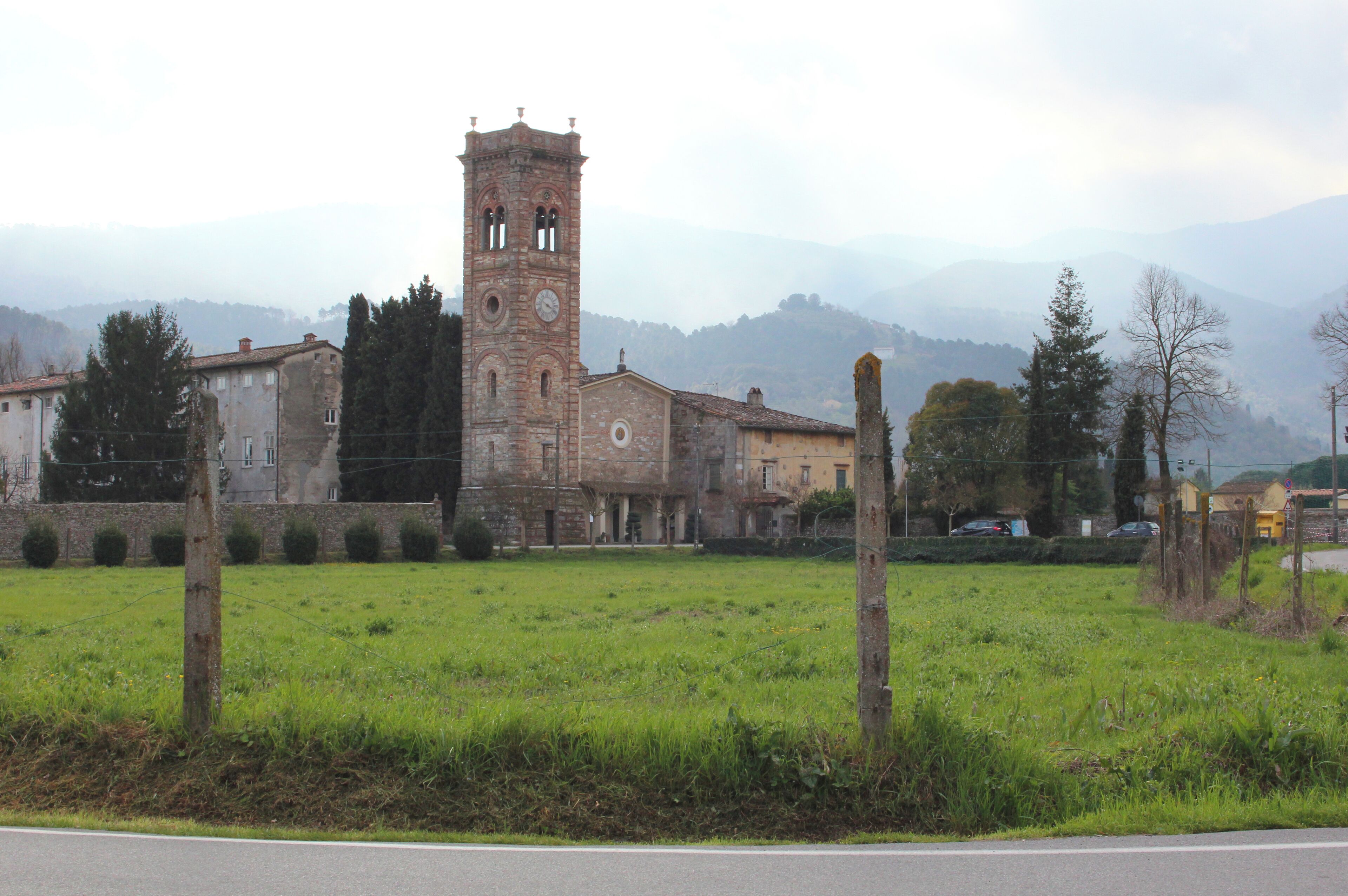 A historic church with a tall bell tower, surrounded by a grassy field and mountains in the background.