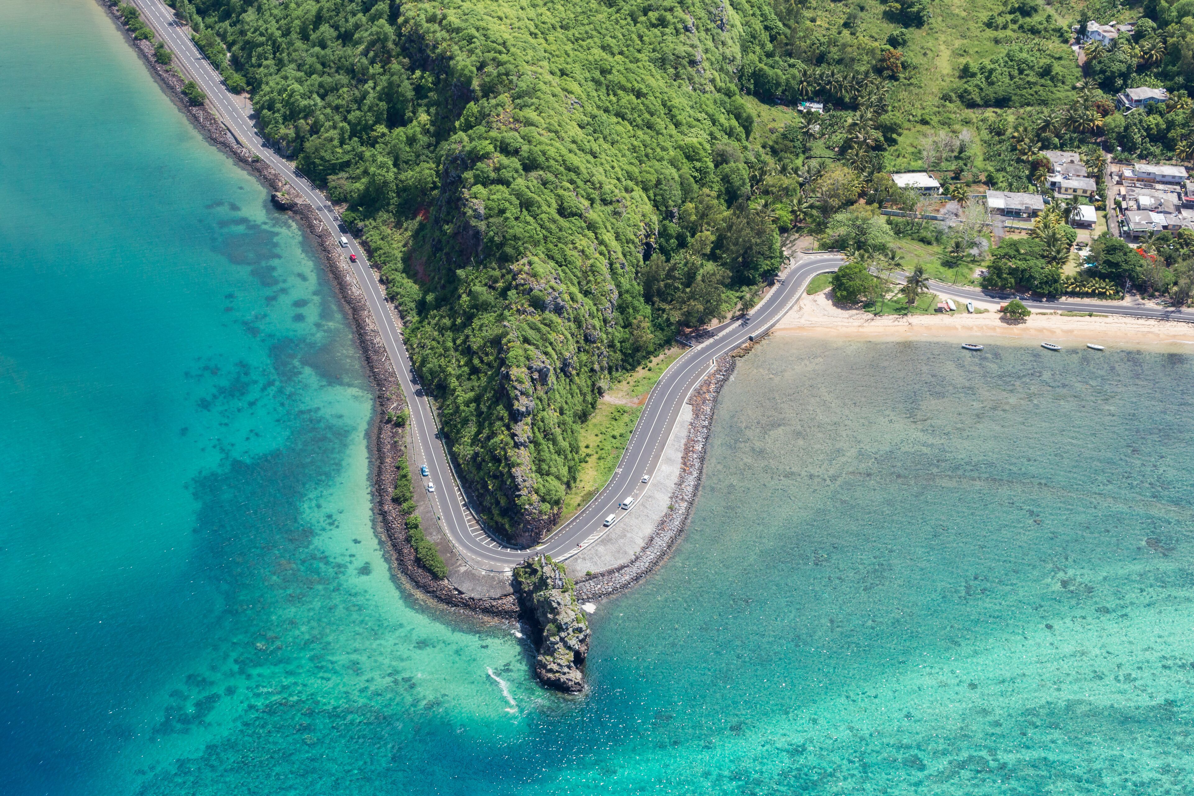 A coastal road curving through a forested area with clear turquoise waters and a rocky outcrop.
