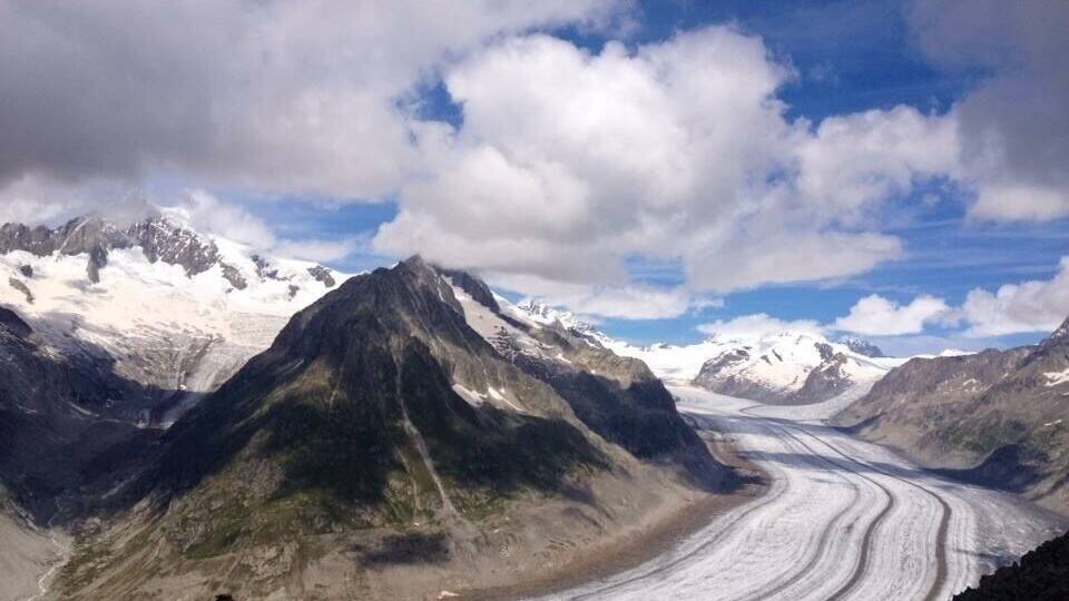 A glacier winding through a mountainous landscape with snow-capped peaks and a clear sky.