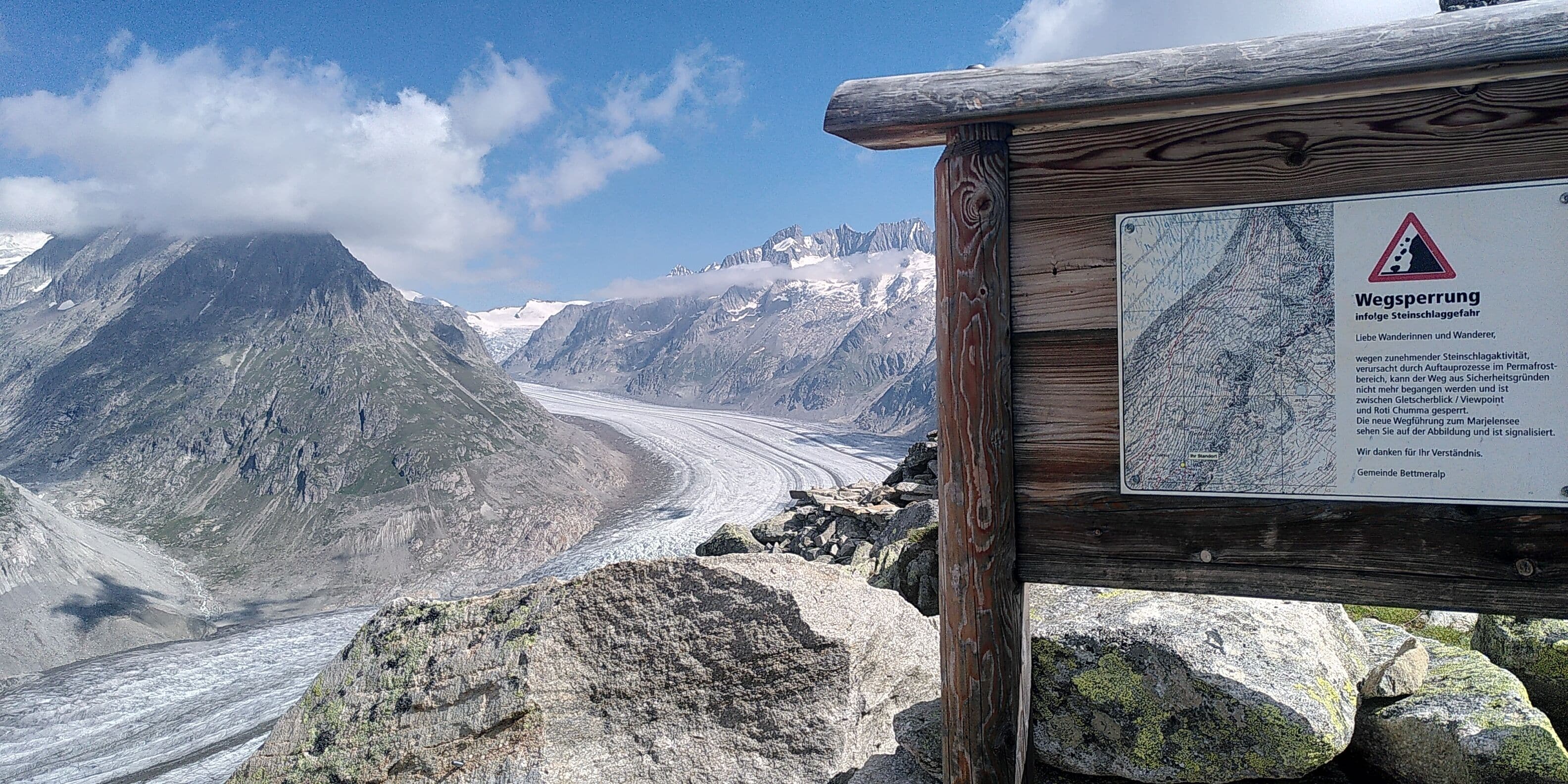 Paisaje montañoso con un glaciar, un cartel de madera y una señal de advertencia.