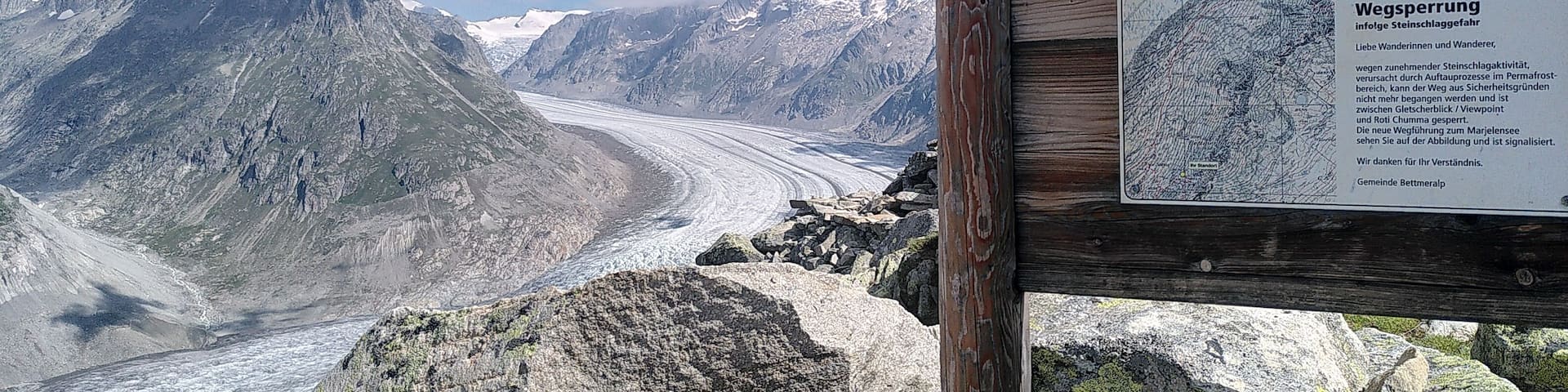 A mountain landscape with a glacier, wooden signpost, and a warning sign.