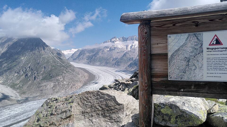 A mountain landscape with a glacier, wooden signpost, and a warning sign.