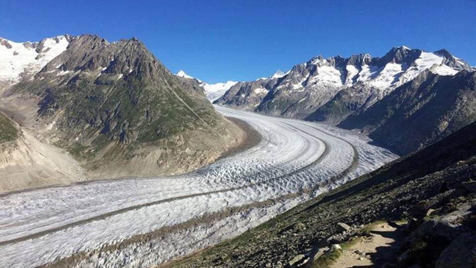 A glacier winding through a mountainous landscape with snow-capped peaks in the background.