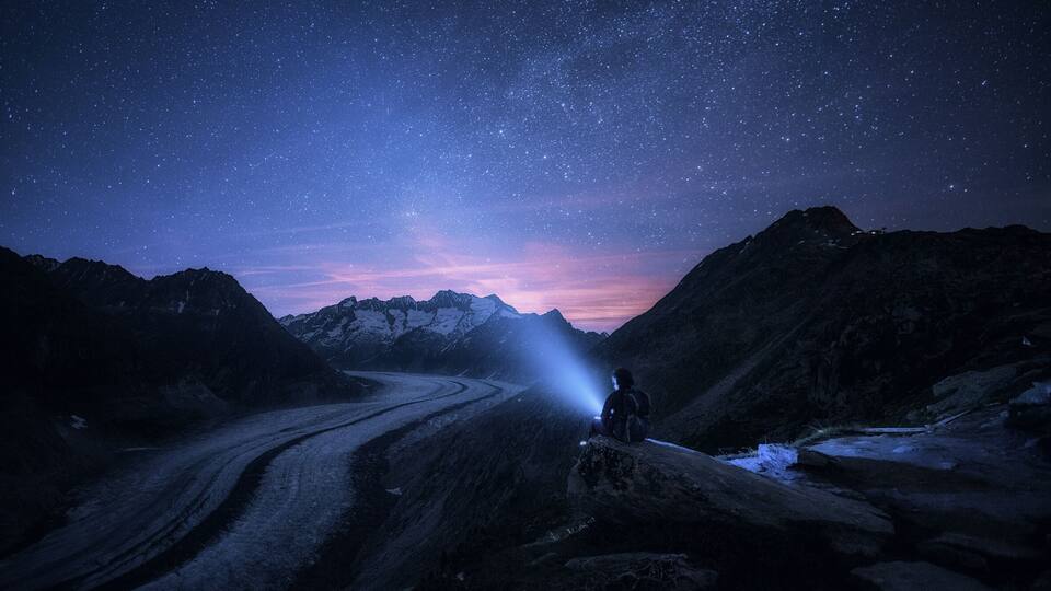 A person with a flashlight in a mountainous landscape at night.