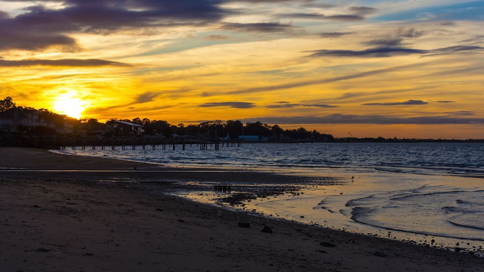 A beach at sunset with a pier extending into the water.
