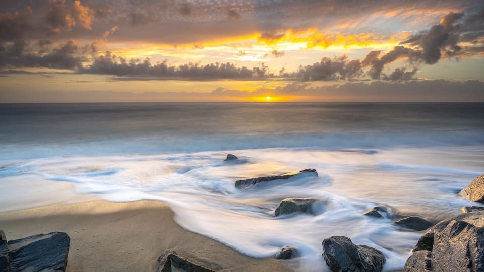 A beach with waves, rocks, and a sunset.