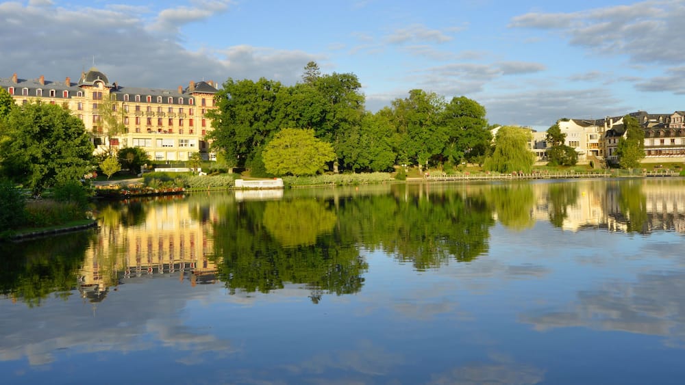 Un lac paisible où se reflètent les bâtiments et les arbres.