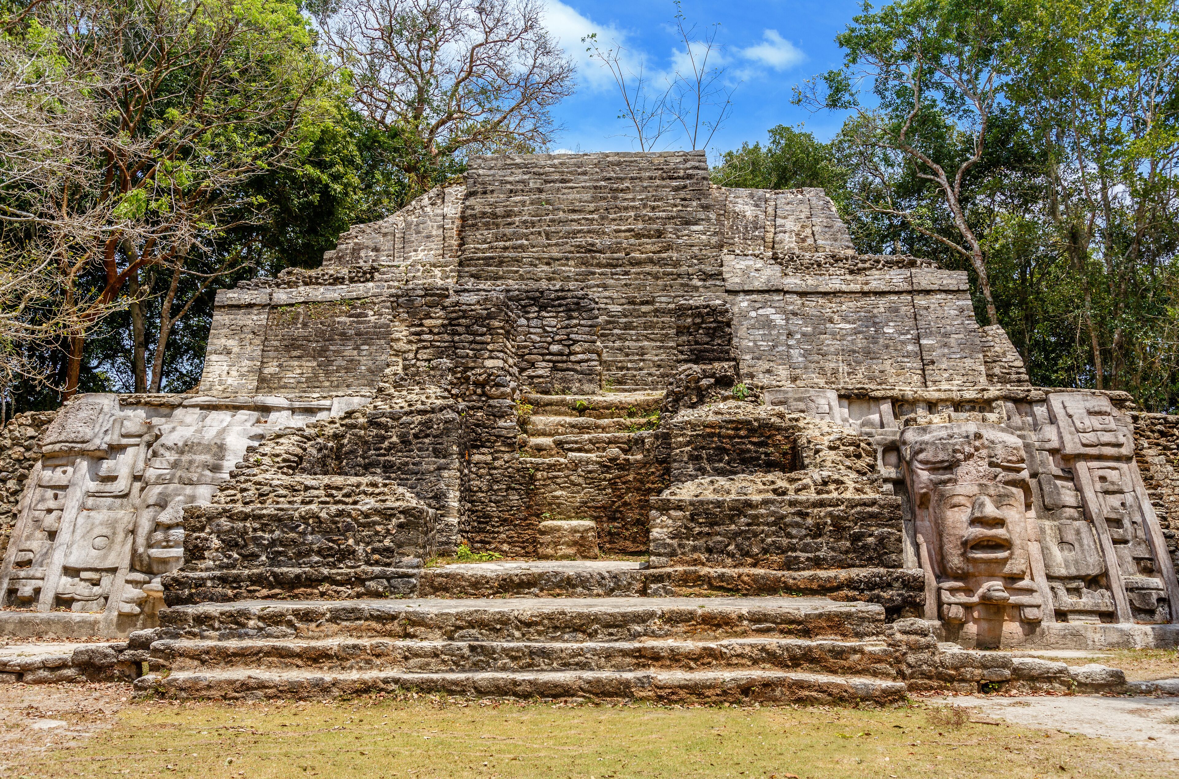 A stone pyramid with steps and intricate carvings, surrounded by trees.