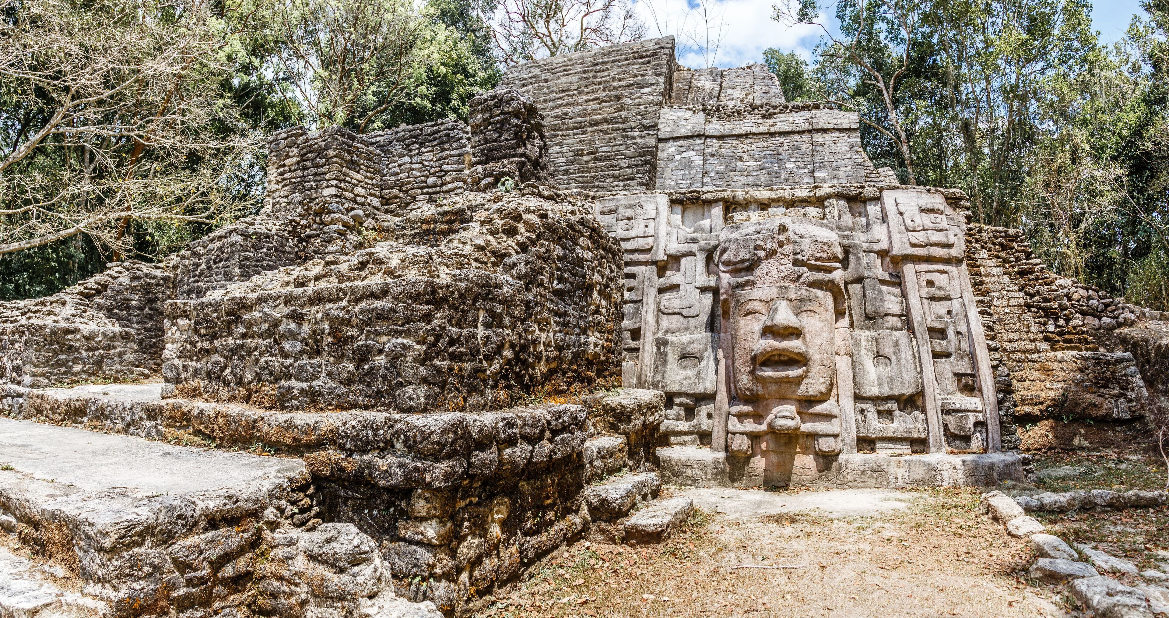 Old ancient stone Mayan pre-columbian civilization pyramid with carved face and ornament hidden in the forest, Lamanai archeological site, Orange Walk District, Belize