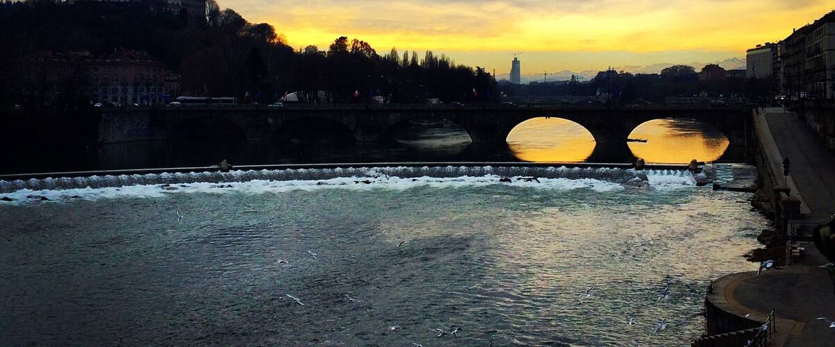 A river with a bridge, a domed building, and a sunset.