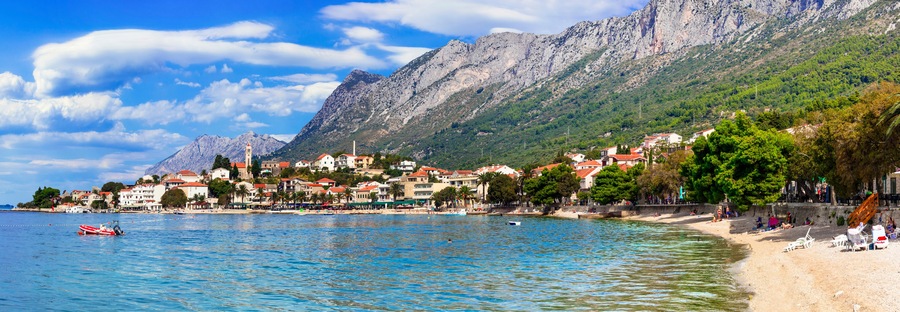 A coastal town with a mountain backdrop, a beach, and a boat in the water.