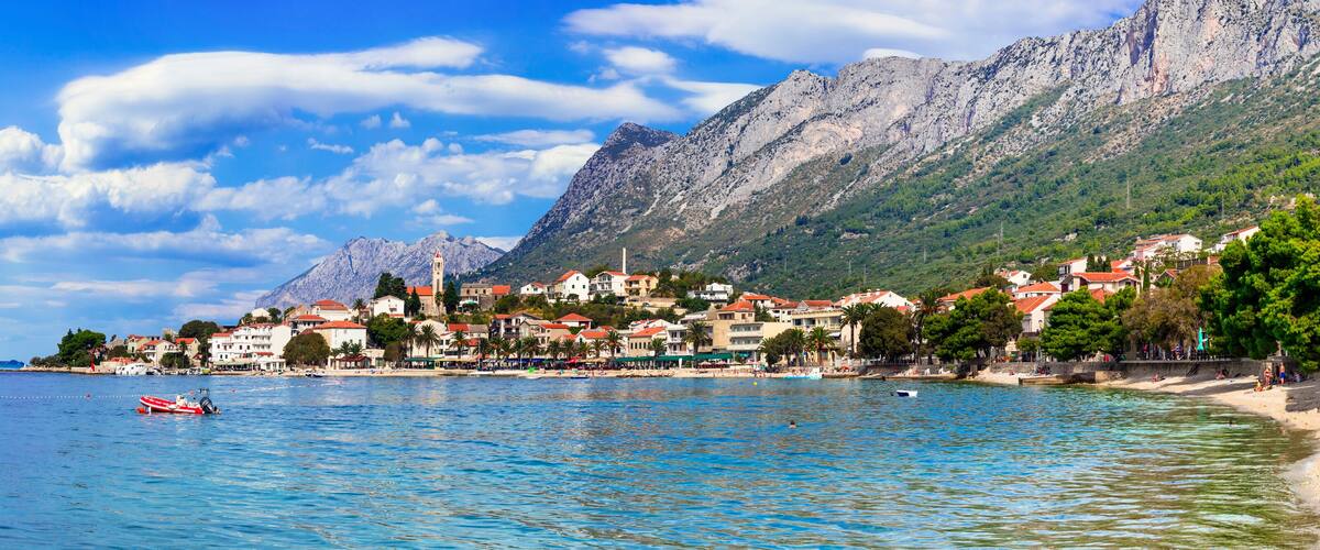 A coastal town with a mountain backdrop, a beach, and a boat in the water.